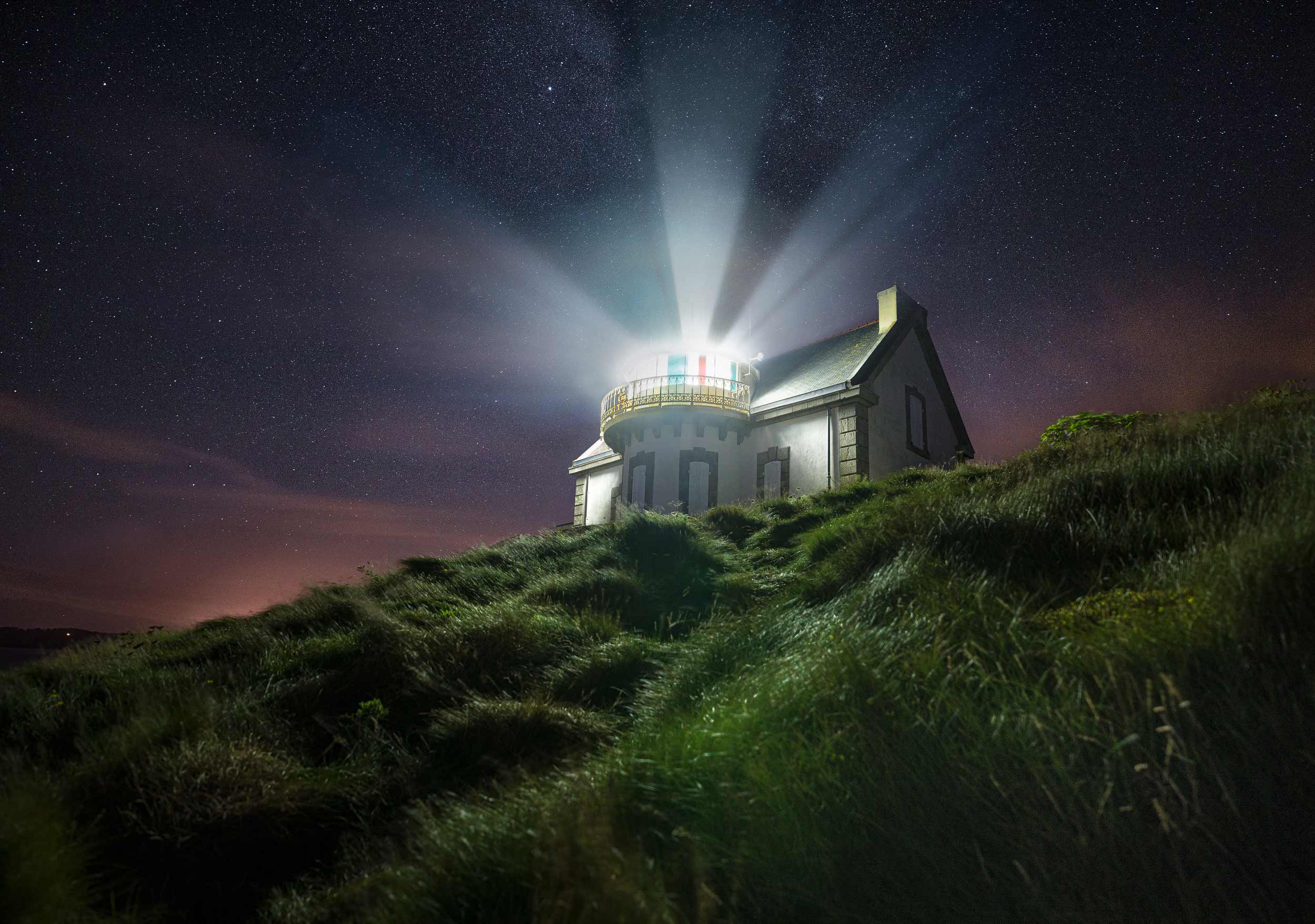 Faro di Millier di notte sotto il cielo stellato con il fascio luminoso della lanterna visibile