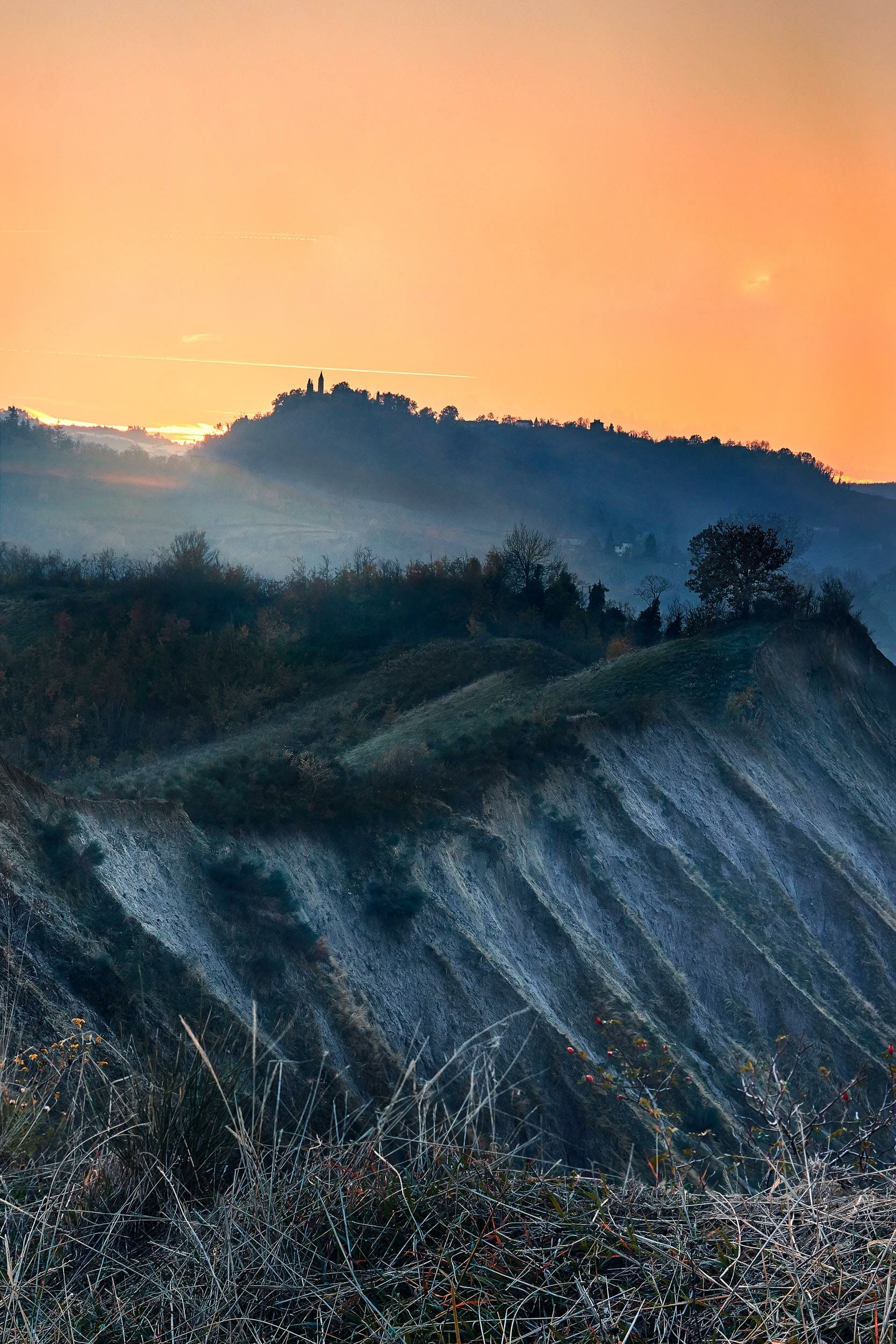 Calanchi al tramonto con una chiesetta su una collina lontana